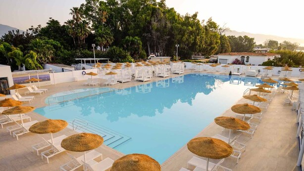 A swimming pool with sun loungers and thatched umbrellas, surrounded by greenery and buildings. - Linda Vista Beach Apartment (Marbella)