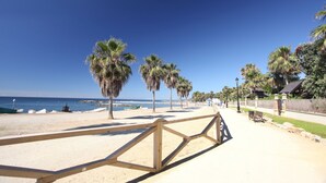 A beach with palm trees, a wooden fence, and a clear blue sky. - Linda Vista Beach Apartment (Marbella)