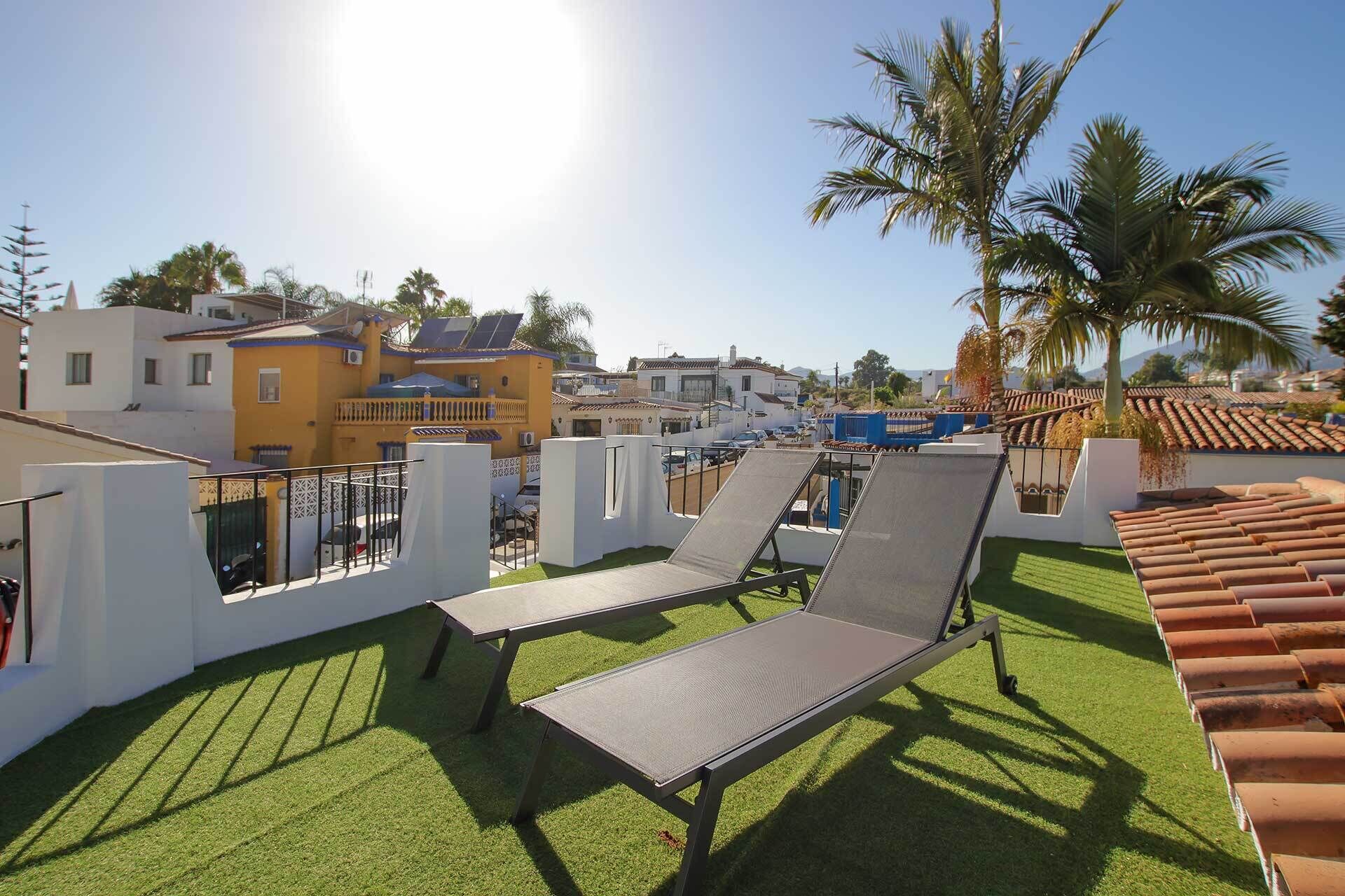 A rooftop with two lounge chairs, a view of residential buildings, and a clear sky.