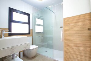 Un baño moderno con cabina de ducha de vidrio, un lavabo blanco y un inodoro.