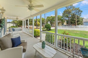 A covered porch with a white railing, a bench, and a wicker sofa with cushions.