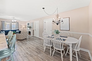 A dining area with a white table and chairs, a chandelier, and a framed quote on the wall.