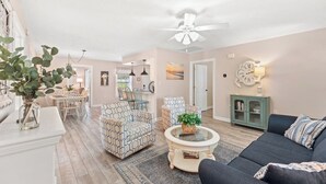A living room with a ceiling fan, patterned chairs, a dark sofa, a coffee table, and a bookshelf. - "Lowery" House w/private pool Free Golf Cart use (North Myrtle Beach)