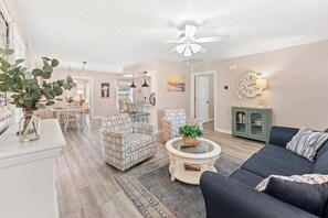 A living room with a ceiling fan, patterned chairs, a dark sofa, a coffee table, and a bookshelf.