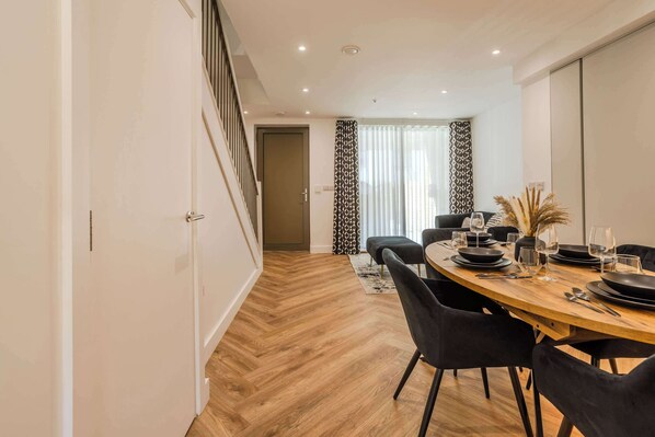 A dining area with a wooden table set for four, black chairs, and a staircase leading to another room.