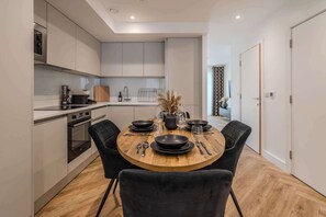 A modern kitchen with built-in appliances, a dining table set for four, and a view into the adjacent living area.