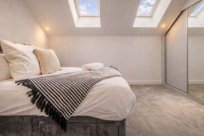 A bedroom with a bed, two skylights, a large mirror, and a carpeted floor.