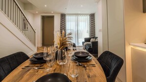 Un comedor con una mesa de madera preparada para cuatro, sillas negras y una escalera a la izquierda.