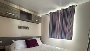 Une chambre à coucher comprenant un lit, une table de chevet, une étagère fixée au mur, une fenêtre avec des rideaux et un luminaire au plafond.