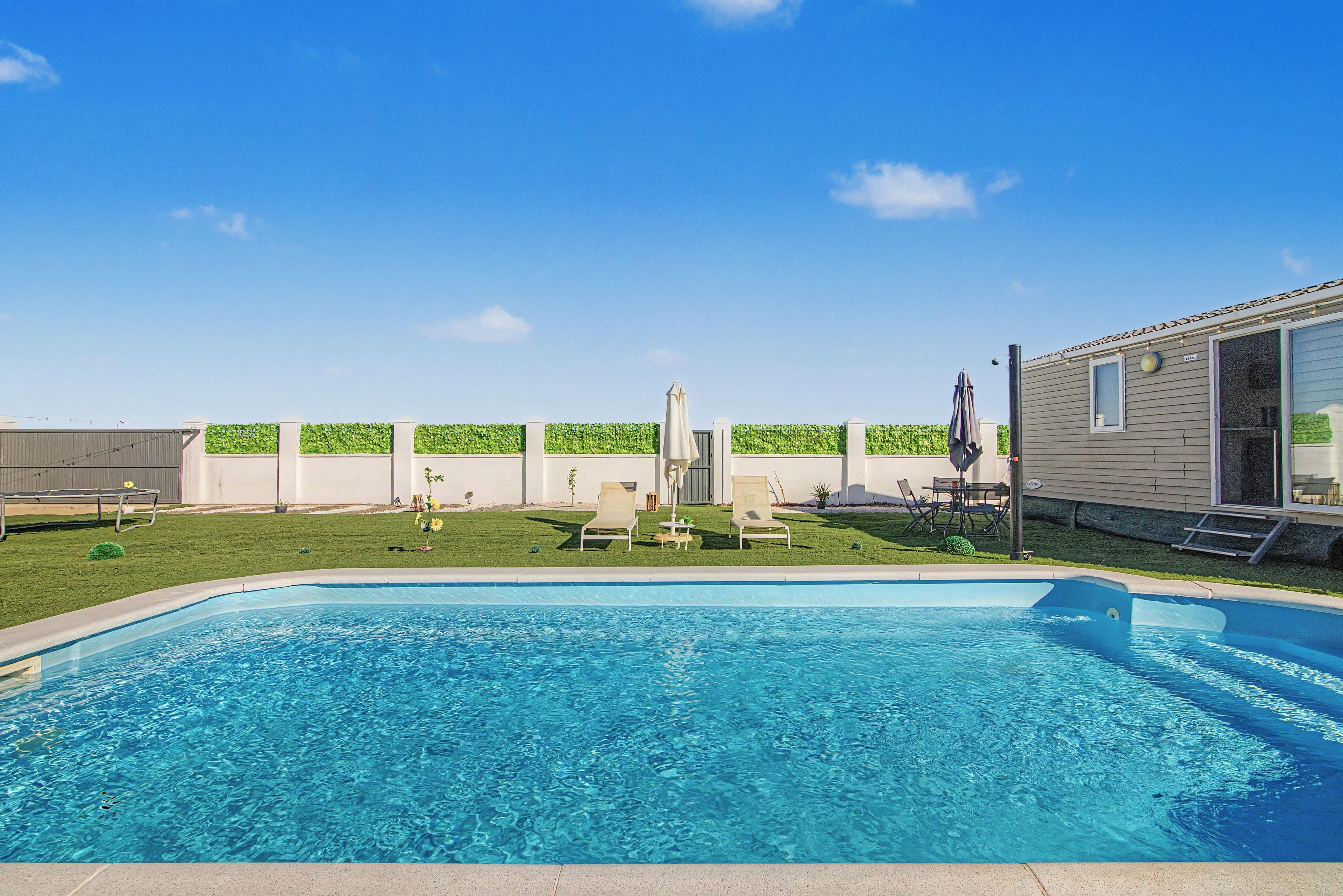 Una piscina con agua cristalina azul, rodeada por un césped y una cerca blanca.