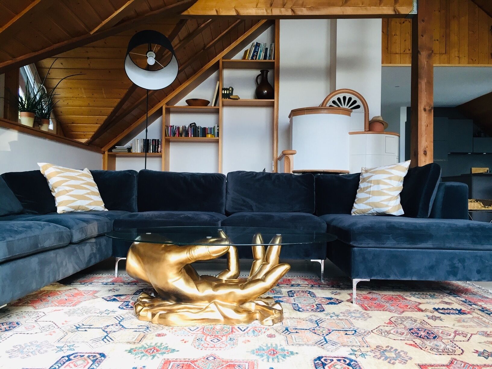 Un salon moderne avec un canapé d’angle bleu foncé, une table basse originale en métal doré aux formes travaillées, et un tapis à motifs.