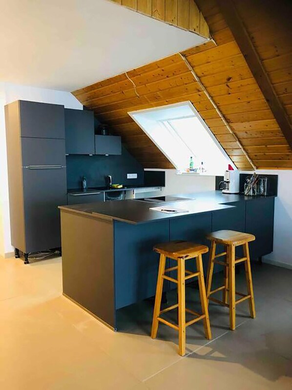 Een moderne keuken met een donkerblauwe keukenbar, houten krukken en een schuine plafond met dakraam.