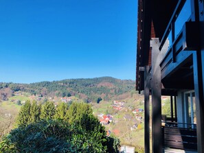 Une vue depuis un balcon donnant sur un village avec ses maisons et une colline boisée.