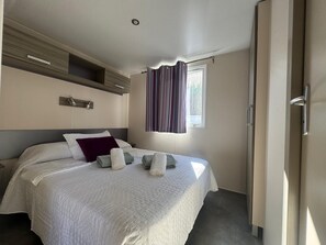 A hotel room with a bed, a window with curtains, a bedside table, and a door.