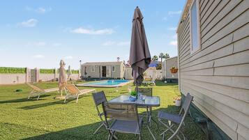 Un patio trasero con piscina, mesa de comedor y sillas, además de una sombrilla.