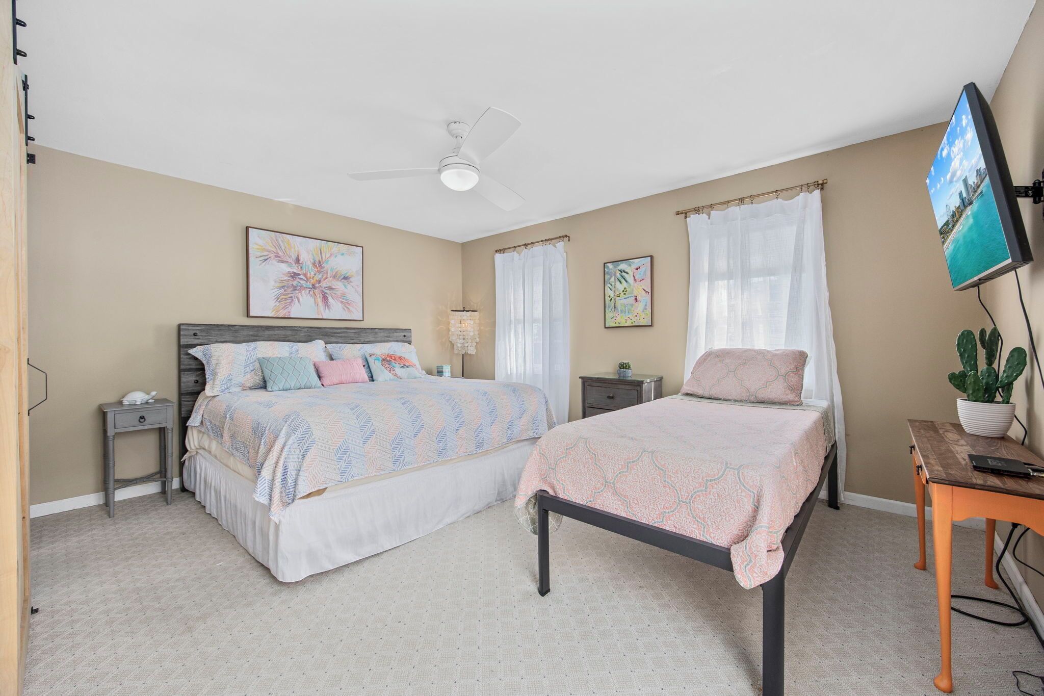 A bedroom with two beds, a ceiling fan, a TV, and a potted plant.