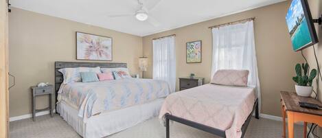 A bedroom with two beds, a ceiling fan, a TV, and a potted plant.