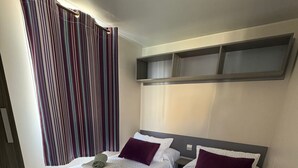 Een hotelkamer met twee éénpersoonsbedden, elk met een kussen en een opgerolde handdoek.