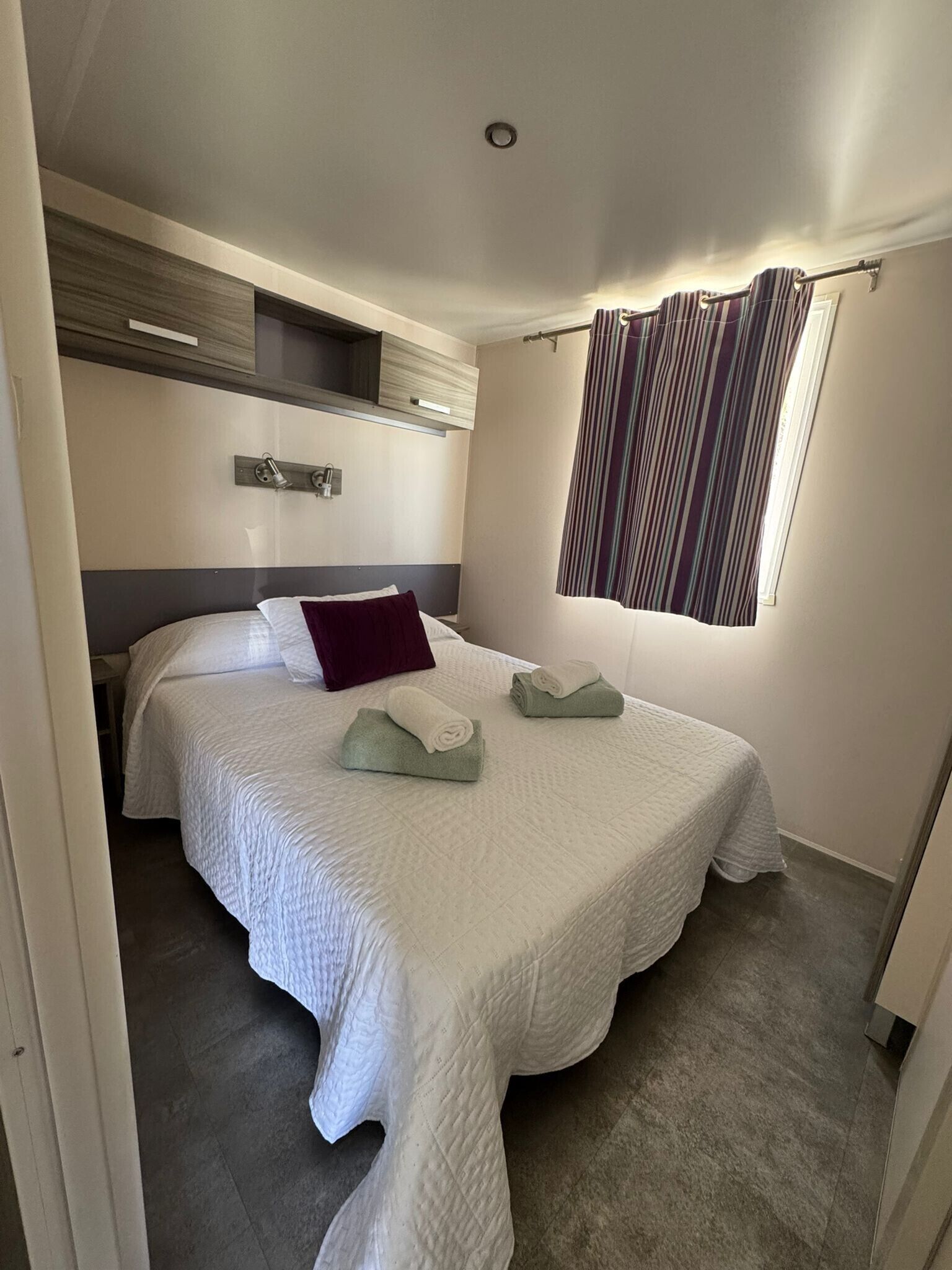 Une chambre à coucher avec un lit, des oreillers, une fenêtre avec des rideaux, une table de chevet et une tête de lit.