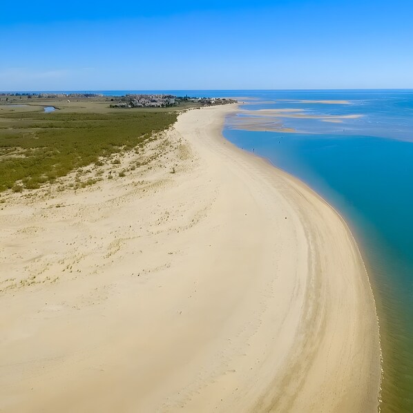 A coastal landscape with a sandy beach, clear blue water, and a distant settlement.