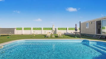 Una piscina con agua cristalina azul, rodeada por un césped y una cerca blanca.