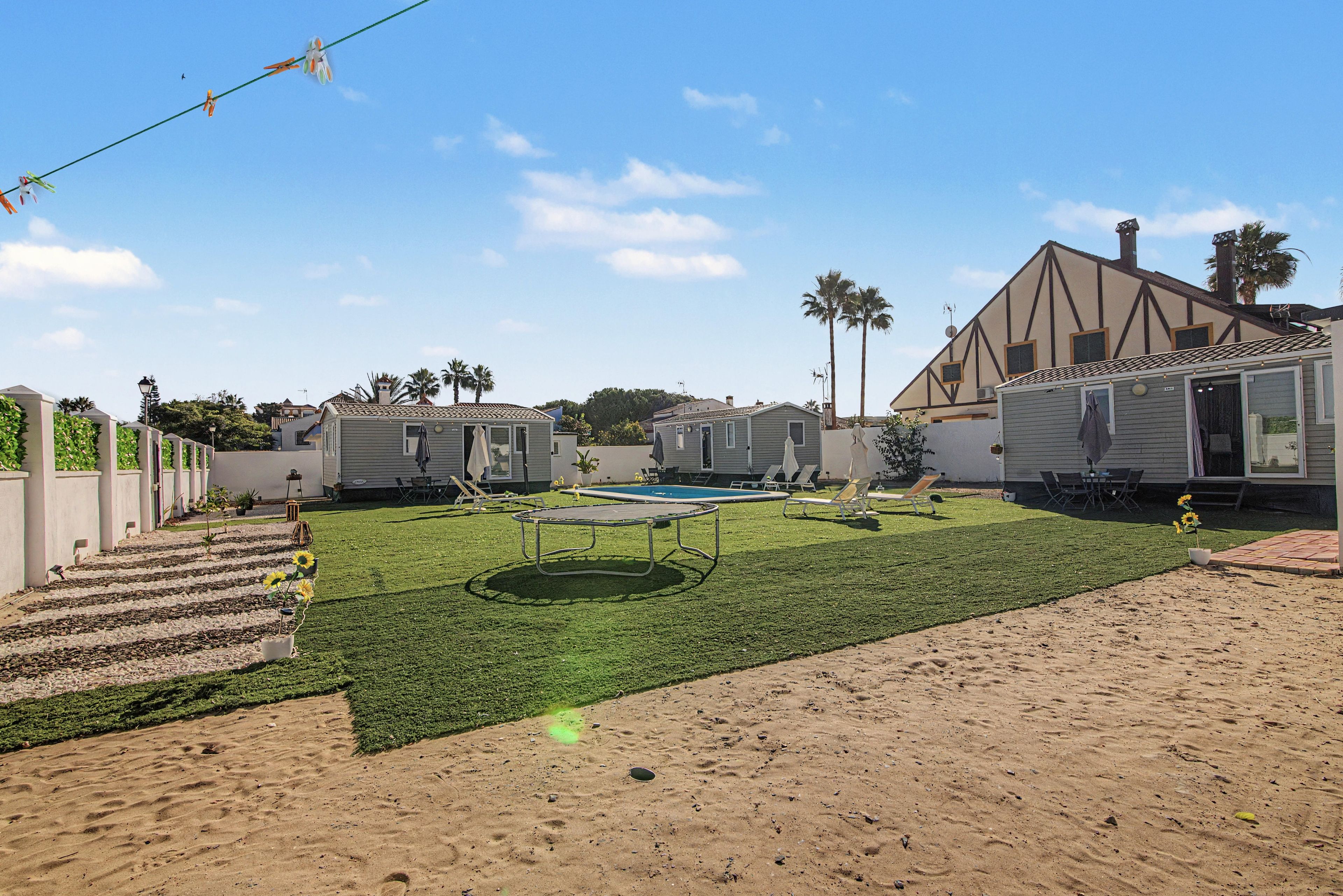 Un barrio residencial con varias casas móviles, una piscina, un trampolín y una zona arenosa.