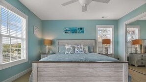 Een slaapkamer met een houten bed, twee nachtkastjes met lampen, een plafondventilator en kunst aan de muur.