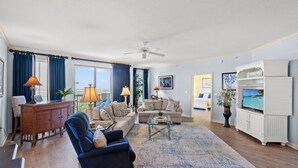 A spacious living room with a large sofa, a coffee table, and a television. There is a ceiling fan, a cabinet with decorative items, and a view of the outdoors through the windows. - Margate 2109 in Kingston, Oceanview, Pool, Beach (Myrtle Beach)