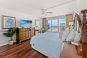Habitación de hotel con cama, televisión, cómoda, escritorio, silla, planta y vista al océano.