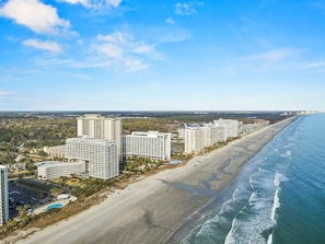 Zona hotelera costera con varios edificios de gran altura, una playa de arena y vistas al océano.
