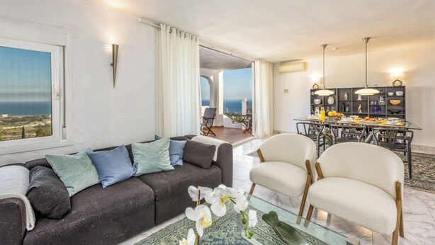 Un soggiorno moderno con un divano, poltrone, un tavolino in vetro e vista mare.