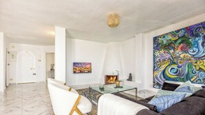 Un soggiorno moderno con un tavolino in vetro, una poltrona bianca, un divano scuro e un quadro astratto dai colori vivaci.