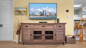 Un salon avec un meuble de rangement en bois servant de support pour l’équipement audiovisuel, un téléviseur à écran plat fixé au-dessus, et un tableau représentant un paysage urbain accroché au mur.