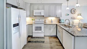 A modern kitchen with white cabinets, a microwave, an oven, a sink, and a coffee maker. - A Place at the Beach A105 New flooring Oceanfront (Myrtle Beach)
