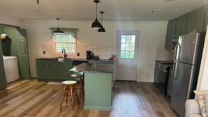 A modern kitchen with green cabinets, a stainless steel refrigerator, wooden stools, and a large window. - Friendly Home Near Downtown UL - Fenced Yard (Lafayette)