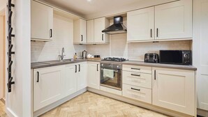 A modern kitchen with white cabinets, a herringbone-patterned floor, a gas stove, a microwave, and a toaster. - Host Stay Holmfirth Hideaway (Holmfirth)