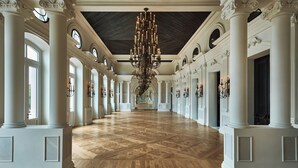 Un vaste hall d’entrée avec de hauts plafonds, des colonnes richement décorées et un grand lustre.