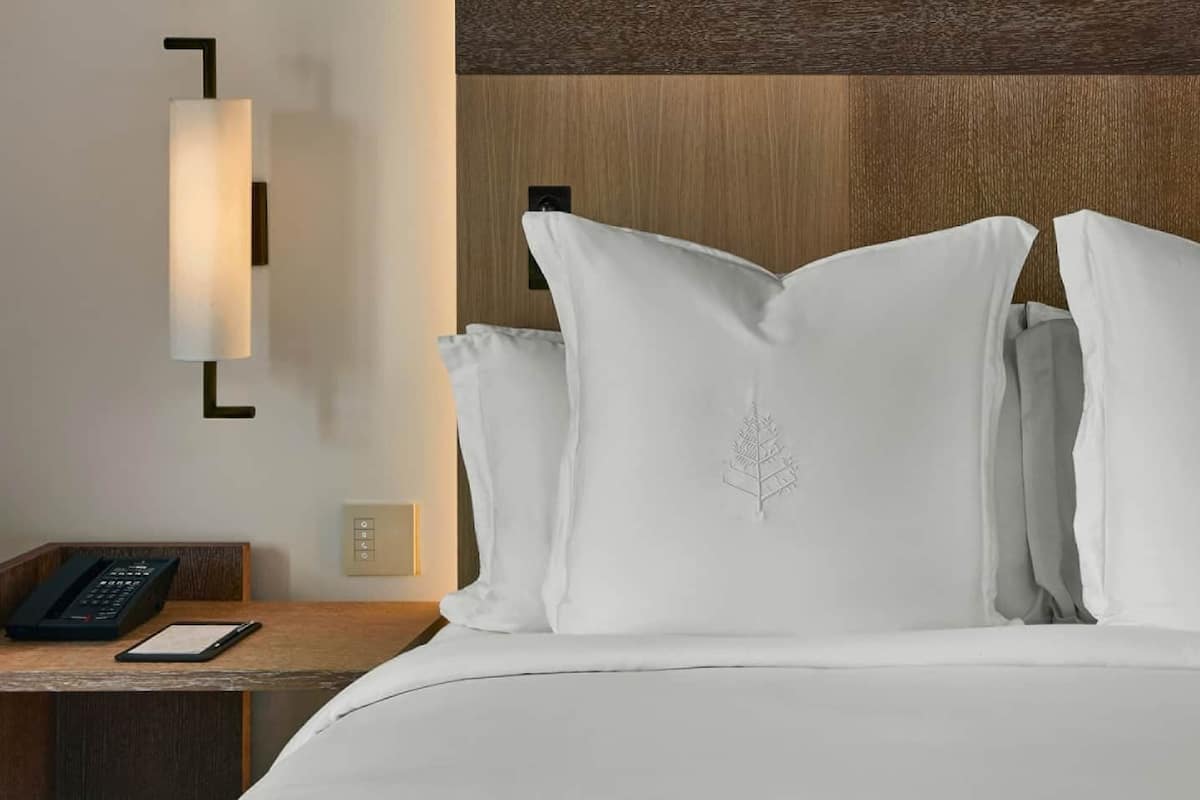 Een hotelkamer met een opgemaakt bed, een telefoon op het nachtkastje en een wandlamp.