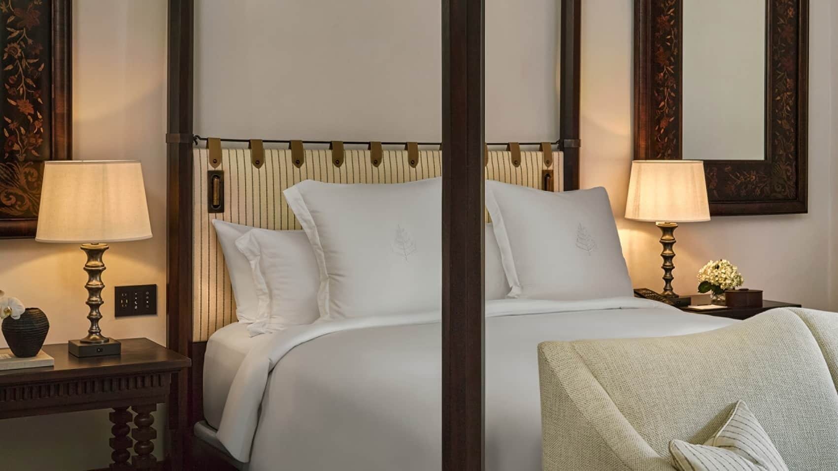Habitación de hotel con una cama grande, dos mesitas de noche con lámparas, un espejo y un jarrón decorativo.