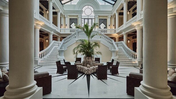 Un vaste hall d’entrée avec un espace salon central, un escalier et une grande plante.