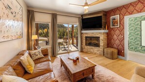 A living room with a leather sofa, a wooden coffee table, a fireplace, and a large TV. - Luxury Condo - Full Spa - Steps to Keystone free shuttle!! (Keystone)