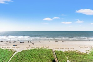 Una playa con un paseo marítimo de madera que conduce al agua, arena y un cielo despejado.