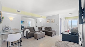 A modern living room with a glass dining table, a sofa set, and a patterned armchair. - San-A-Bel #501 Adorable Oceanfront End Unit (North Myrtle Beach)