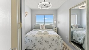 A bedroom with a bed, a window with a view of the ocean, a mirror, and a ceiling light fixture. - San-A-Bel #501 Adorable Oceanfront End Unit (North Myrtle Beach)