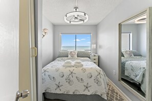 Ein Schlafzimmer mit Bett, Fenster mit Meerblick, Spiegel und Deckenleuchte.
