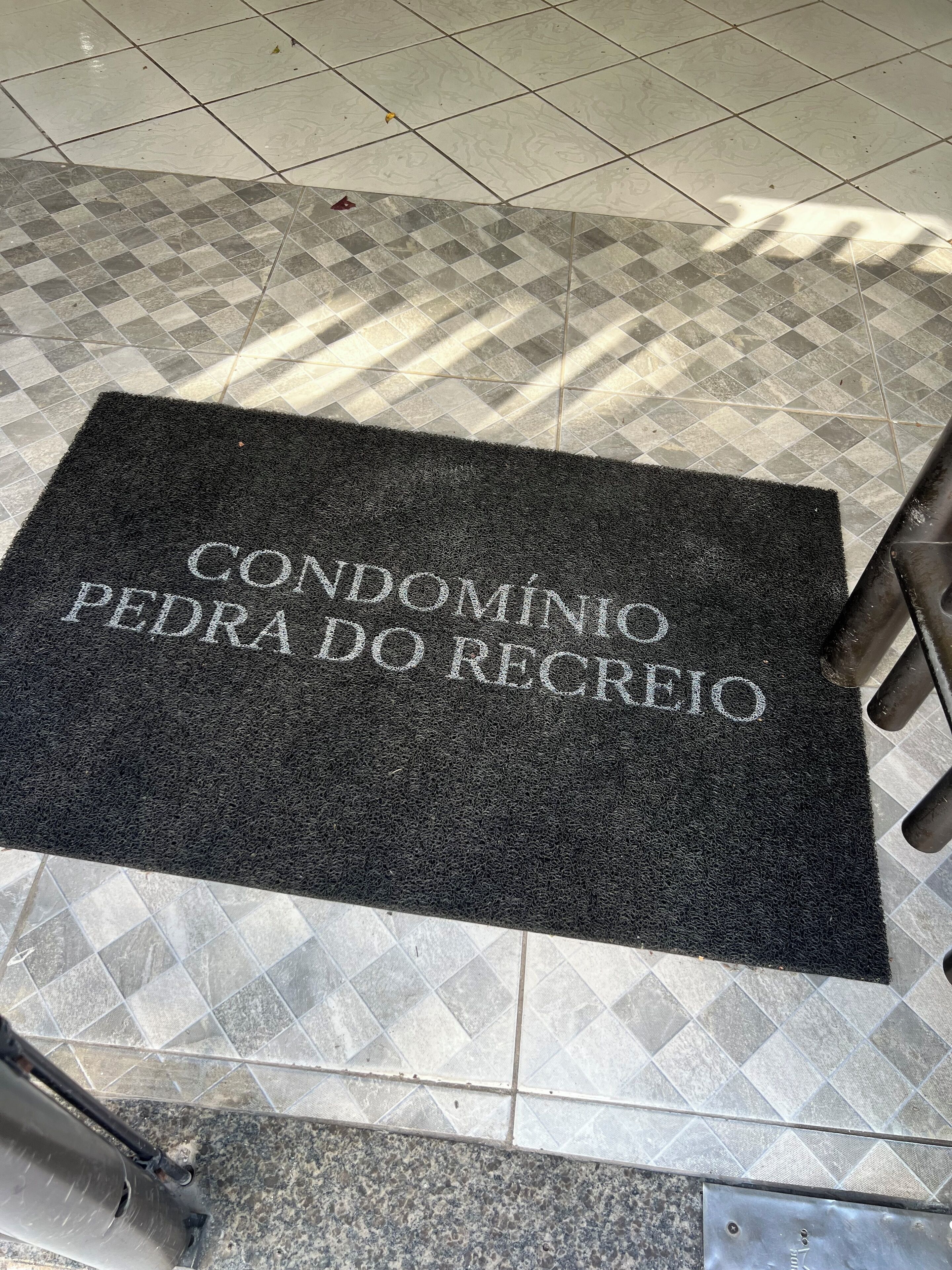 Eine schwarze Fußmatte mit dem Aufdruck "CONDOMÍNIO PEDRA DO RECREIO" auf gefliestem Boden.