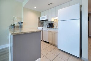 A modern kitchen with white cabinets, a granite countertop, a built-in dishwasher, and a stainless steel refrigerator.
