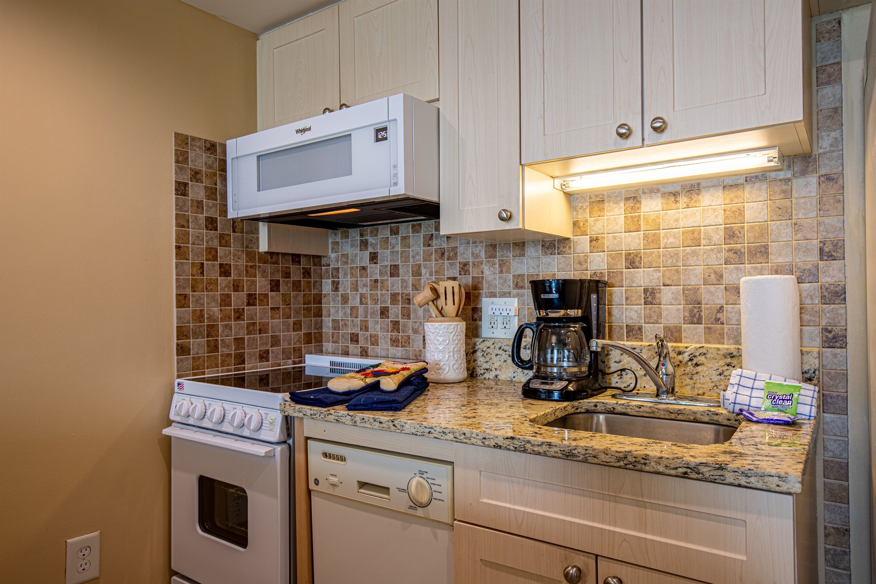 A compact kitchen with a microwave, stove, dishwasher, and coffee maker.