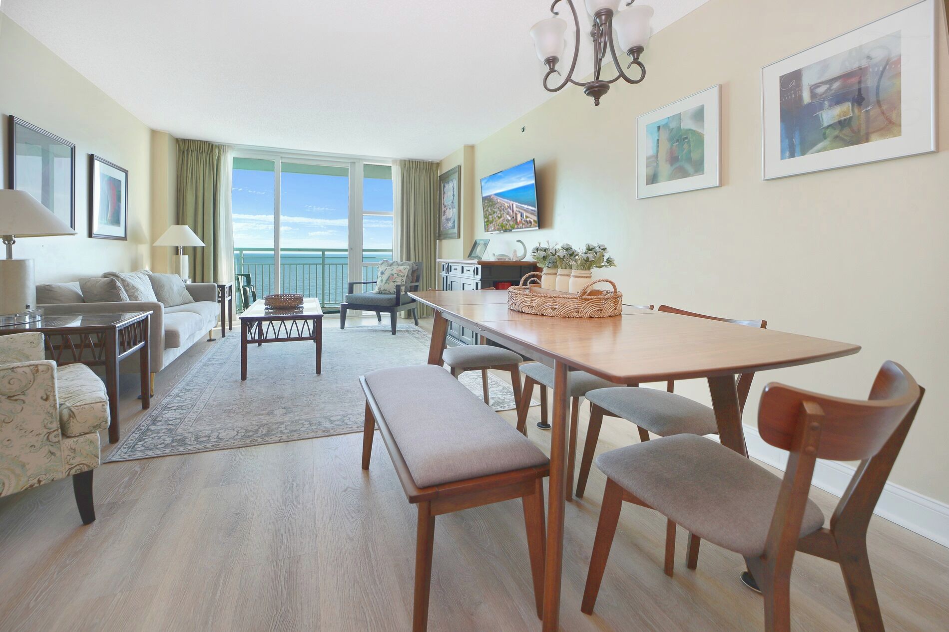 A spacious living room with a balcony, a dining area, and a TV mounted on the wall.