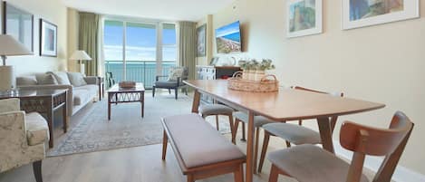 Un salón amplio con balcón, una zona de comedor y un televisor montado en la pared.